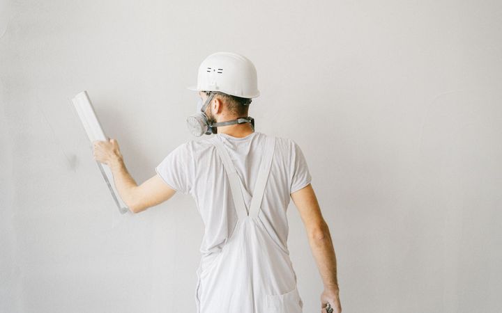 Worker in a respirator and hard hat smoothing compound on a white wall